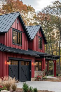 a red house with black garage doors and windows on the front, surrounded by trees