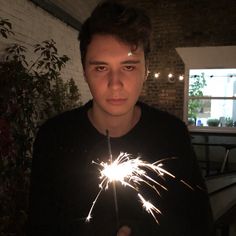 a young man holding a sparkler in his right hand and looking at the camera