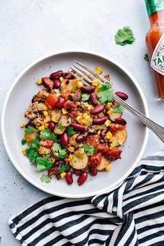 a white plate topped with corn, tomatoes and cucumbers next to a spoon