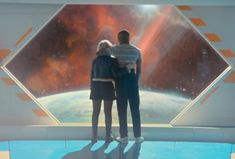 two people standing next to each other in front of a large window looking at the space