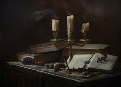 an open book with two candles on top of it next to some books and pine cones