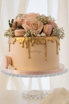 a cake with icing and flowers on top sitting on a table next to a white curtain