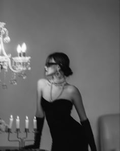 a woman in a black dress standing next to a chandelier