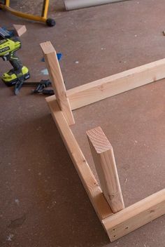 an unfinished bed frame sitting on top of a floor next to a driller and screwdriver