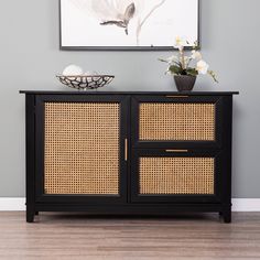 a black cabinet with wicker doors and drawers in front of a painting on the wall