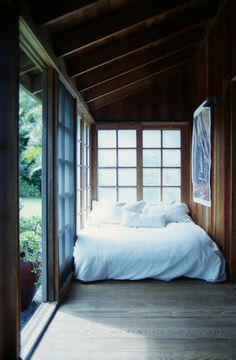 a bed sitting inside of a bedroom next to an open window on top of a wooden floor