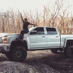 a man sitting on the back of a white truck with his arms in the air