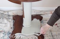 someone is painting the base of a table with white paint on it and peeling from the top