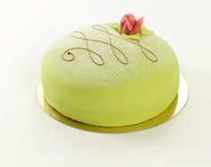 a green cake with white frosting and a pink flower on top, sitting on a gold platter