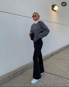 a woman standing in front of a white wall with her hands on her hips and wearing black pants