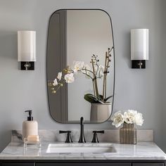 a bathroom sink with a large mirror above it and flowers in a vase on the counter