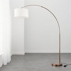 a floor lamp with a white shade on it in a room next to a window