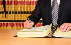 a man in a suit and tie sitting at a desk writing on an open book