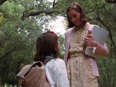 two young women walking through the woods with backpacks on their back and one holding a book