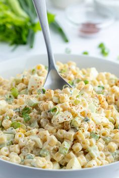 a white bowl filled with macaroni salad on top of a table next to lettuce