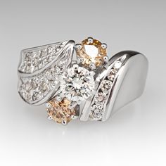 This lovely three-stone diamond ring is centered with one (1) round brilliant cut diamond set into a six- prong setting and flanked to each side by one (1) old European cut fancy light brown colored diamond set into a six-prong setting. The shoulders of the ring are accented with diamonds. One shoulder is bead set with nineteen (19) round single cut diamonds and one (1) round brilliant cut diamond. The other shoulder is channel set with five (5) round brilliant cut diamonds. The ring measures 13.1mm at the top, rises 6.8mm above the finger, tapering to 2.9mm wide and 1.1mm thick at the base of the shank. It is currently a size 6. Several of the diamonds are lightly chipped. Brown Diamond Ring Fine Jewelry, Classic Brown Diamond Jewelry, Brown Diamond Ring With Diamond Accents For Anniversary, Brown Diamond Ring With Accents For Anniversary, Brown Diamond Jewelry For Anniversary, Anniversary Brown Diamond Ring With Accents, Elegant Brown Diamond Ring, Anniversary Brown Diamond Jewelry, Brown Prong-set Ring For Anniversary