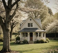 a small white house sitting in the middle of a lush green field next to trees