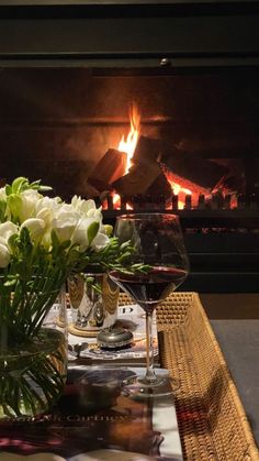 a table with flowers and wine glasses on it in front of an open fire place