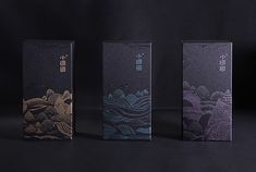 three boxes with designs on them sitting in front of a black background, one is blue and the other is purple