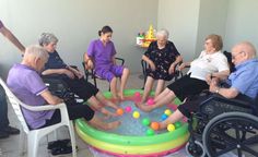 several elderly people sitting in chairs around an inflatable pool with balls on it