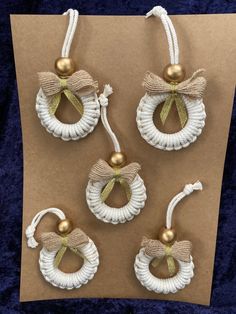 four white and gold christmas ornaments hanging from strings on a brown paper sheet with blue velvet background