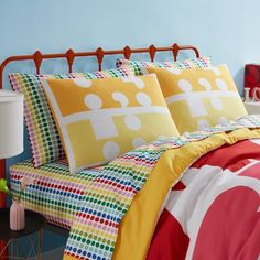 a bed with colorful sheets and pillows on top of it next to a night stand