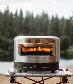 a toaster oven sitting on top of a camping table next to a body of water