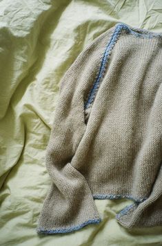 a sweater laying on top of a bed covered in white sheets and blue trims