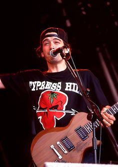 a man holding a guitar while standing next to a microphone on top of a stage