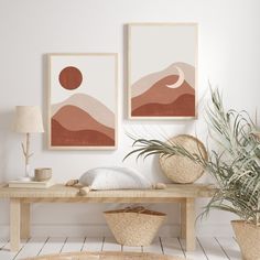 two paintings hang on the wall next to a wooden table with baskets and plants in front of it