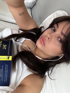 a woman laying on top of a bed with headphones in her ears and reading a book