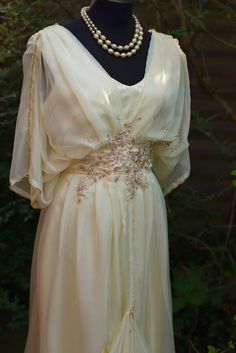 Here is my buttercream chiffon and satin draped evening dress, inspired by the elegant style of the 20s and 70s. This unique design is perfect for romantic weddings, proms, or any special occasion. The dress features delicate, silky buttercream chiffon that drapes beautifully and is fully lined with ivory satin for a luxurious and comfortable feel. It's beautifully finished with gold embroidery, gold beading, faux pearls, and vintage lace accents, adding a touch of glamour and vintage charm. . T Luxury Vintage Dress For Costume Events, Luxury Romantic Vintage Costume Dress, Luxury Romantic Cream Gown, Luxury Vintage Dress With Ruched Bodice, Luxury Romantic Victorian Dress For Vintage Events, Luxury Spring Vintage Dress For Women, Luxury Elegant Cream Evening Dress, Luxury Romantic Cream Dress, Luxury Elegant Cream Victorian Dress