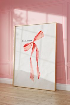 a pink room with a white framed poster on the wall and a red ribbon tied to it