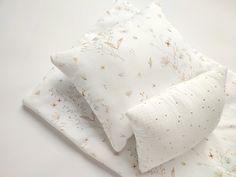 two white pillows on top of each other next to a pillow case with floral designs