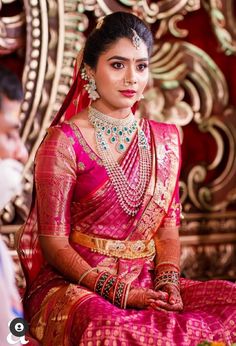 a woman in a red and gold sari sitting on a chair with her hands clasped to her chest