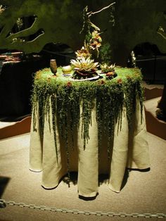 a table covered in plants and greenery on top of a carpeted floor next to a tree