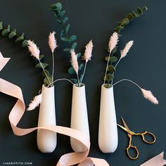 three vases with flowers in them and some ribbon on the table next to it