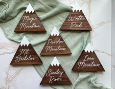 four wooden coasters with the names of five different mountain peaks on them, sitting next to a green towel