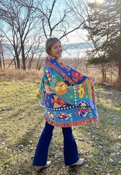 a woman is walking in the grass wearing a colorful shawl