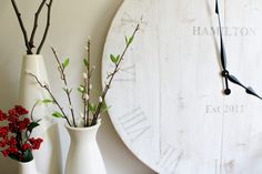 two white vases with flowers in them are next to a clock on the wall