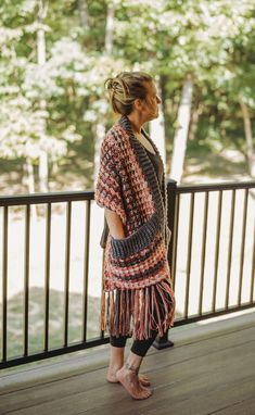 a woman is standing on a porch with her back to the camera, wearing a crocheted shawl and sandals