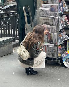 a woman kneeling down next to a pile of newspapers