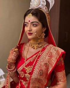 a woman in a red and gold bridal outfit holding a piece of jewelry on her left hand