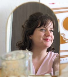 a woman sitting in front of a mirror looking into the camera with her eyes closed