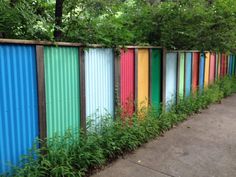 a row of multicolored metal fences next to a sidewalk in front of trees