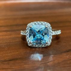 a ring with an aqua blue topaz surrounded by diamonds on a wooden surface,