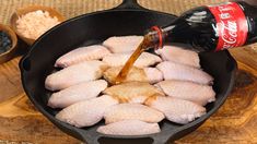 chicken being poured into a skillet with other ingredients on the side and an empty coke bottle