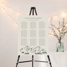 a wedding seating chart is displayed on a easel with lights in the background and a vase full of flowers