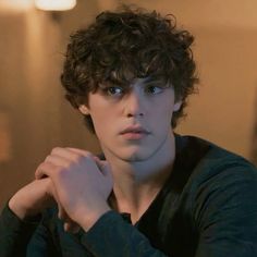 a young man with curly hair wearing a black shirt and looking at the camera while holding his hand on his shoulder