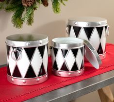 two black and white tin canisters sitting on top of a red table next to a christmas tree